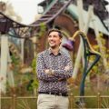 robbert-eggers Man smiling outdoors at Plopsa amusement park with roller coaster in background.